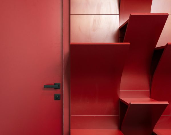 Interior of modern office with red door next to empty shelves near wall
